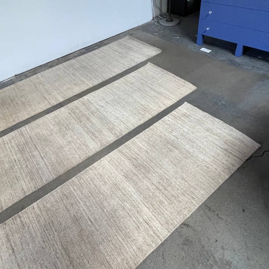Three beige Delinear wool runners with dark borders on a concrete floor in a garage setting.