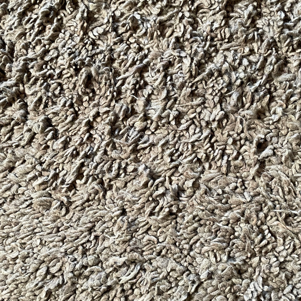 Close-up view of the corner of a Delinear Anemone Warm Grey 8'X10' Shag Rug, crafted from luxurious Himalayan wool, against a plain white background.