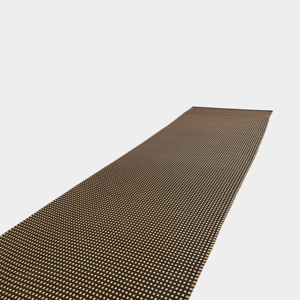 An indoor/outdoor Woodnotes City Rug with cozy detail, in black and tan, on a white surface.