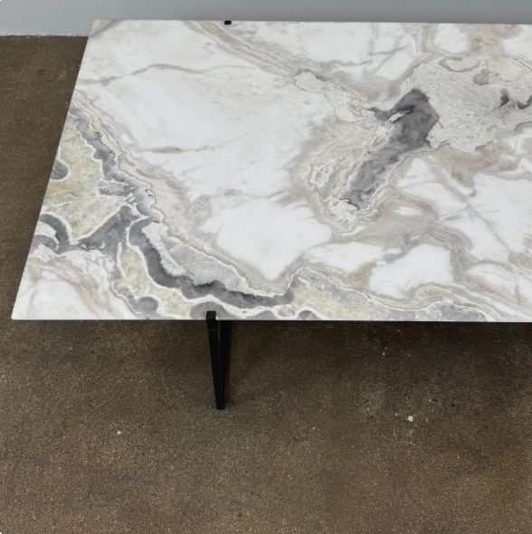 Rectangular table with a white and gray marble-patterned top and black metal legs, placed on a concrete floor.
