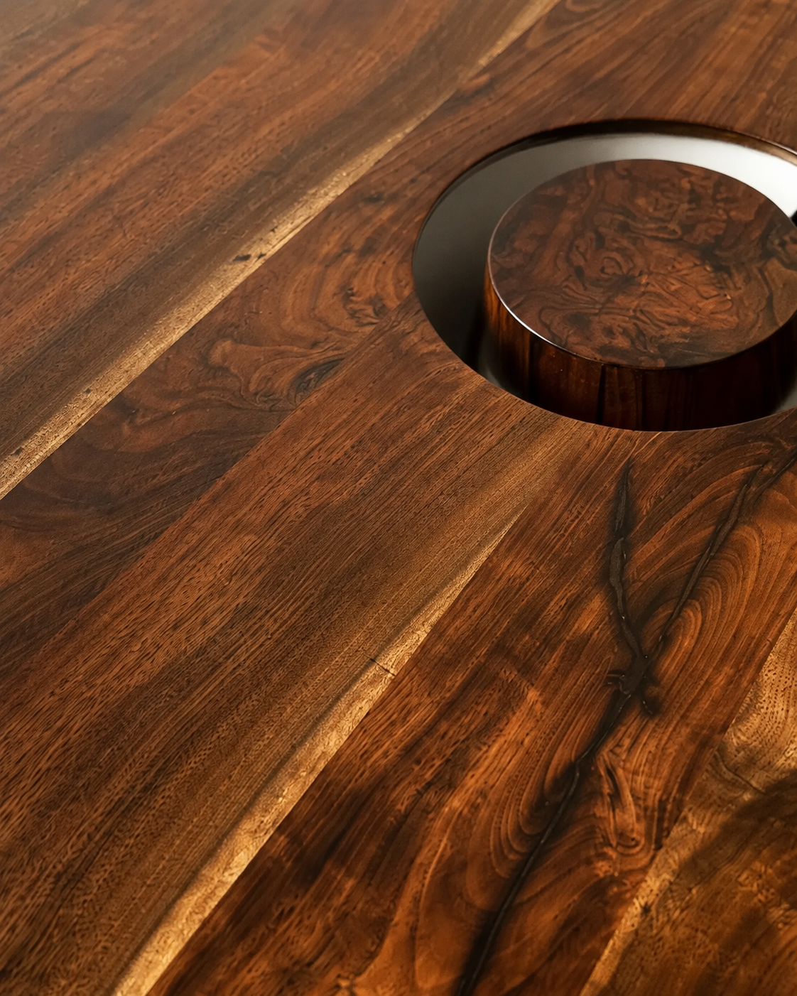 Close-up of a polished wooden table with a circular inset feature, showcasing natural wood grain patterns and textures.