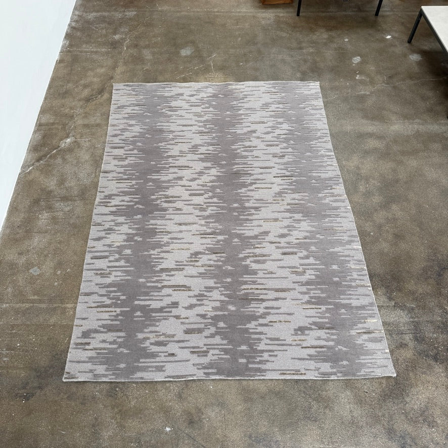 A close-up of the Kvadrat Multi-pile Wool and Silk Rug by Kvadrat, featuring an abstract linear pattern in light and dark gray wool and silk, displayed on a white background.