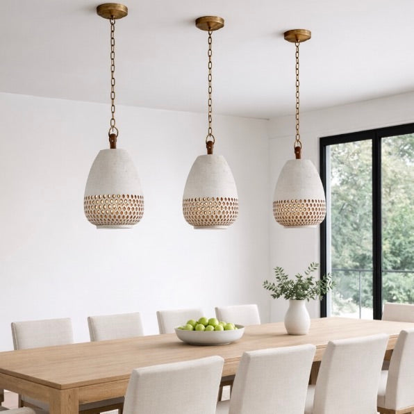 The L’aviva Diamantes Pendant Light, Size B by L’aviva features a white ceramic shade with hand-cut clay patterns, inspired by Oaxacan pottery, and hangs in a modern room with art and contemporary furniture.