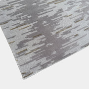 A close-up of the Kvadrat Multi-pile Wool and Silk Rug by Kvadrat, featuring an abstract linear pattern in light and dark gray wool and silk, displayed on a white background.