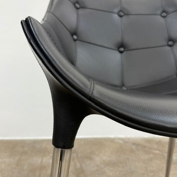 The Cassina Passion Side Chair by Cassina is a modern black upholstered chair with a curved backrest, button detailing, and four sleek metal legs inspired by the Passion design.