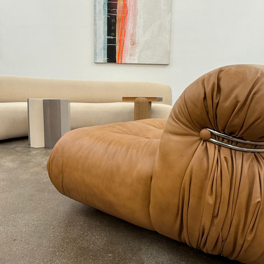 A set of two tan leather lounge chairs, echoing the vintage 1970s Cassina Soriana designs by Afra & Tobia Scarpa, showcases tufted backrests and tubular metal frames on a plain white background.