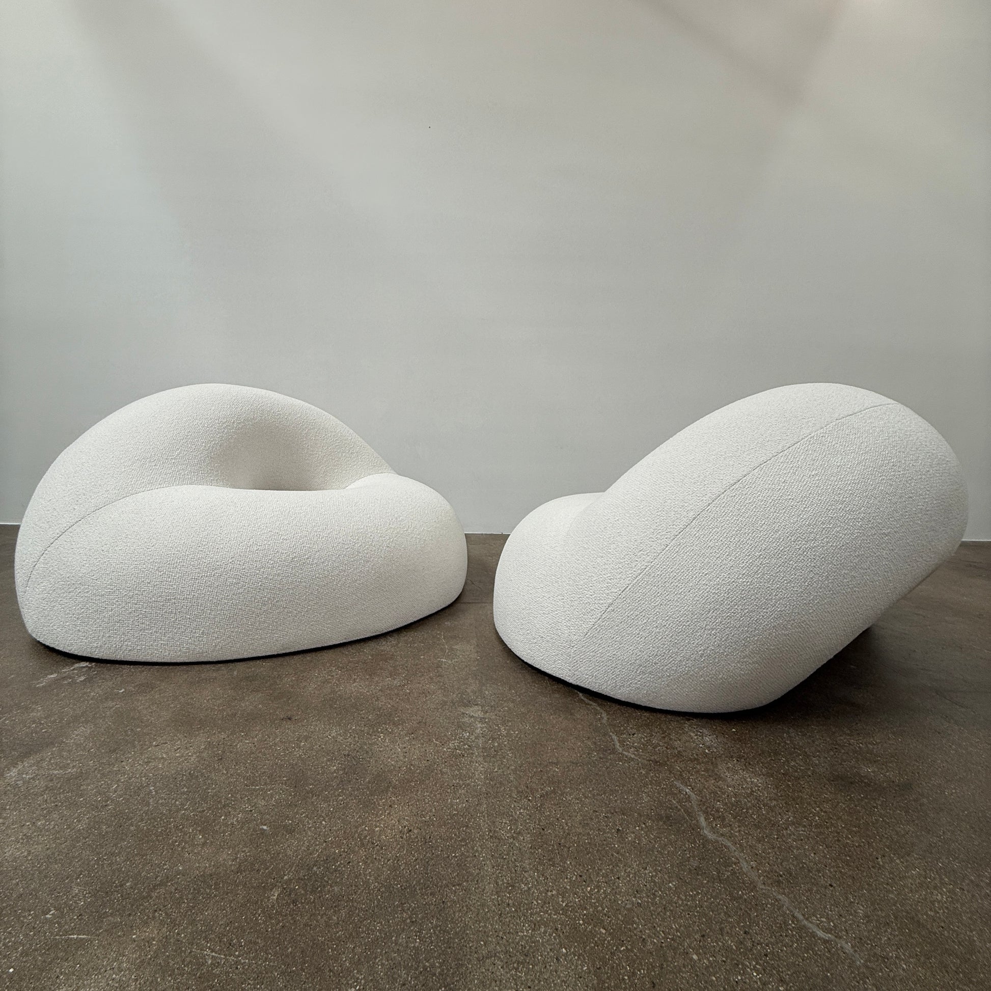 The Objects of Common Interest Tube Chair by Objects of Common Interest is a modern, light grey lounge chair with a donut-shaped design, rounded form, and central indentation, shown against a plain white background.