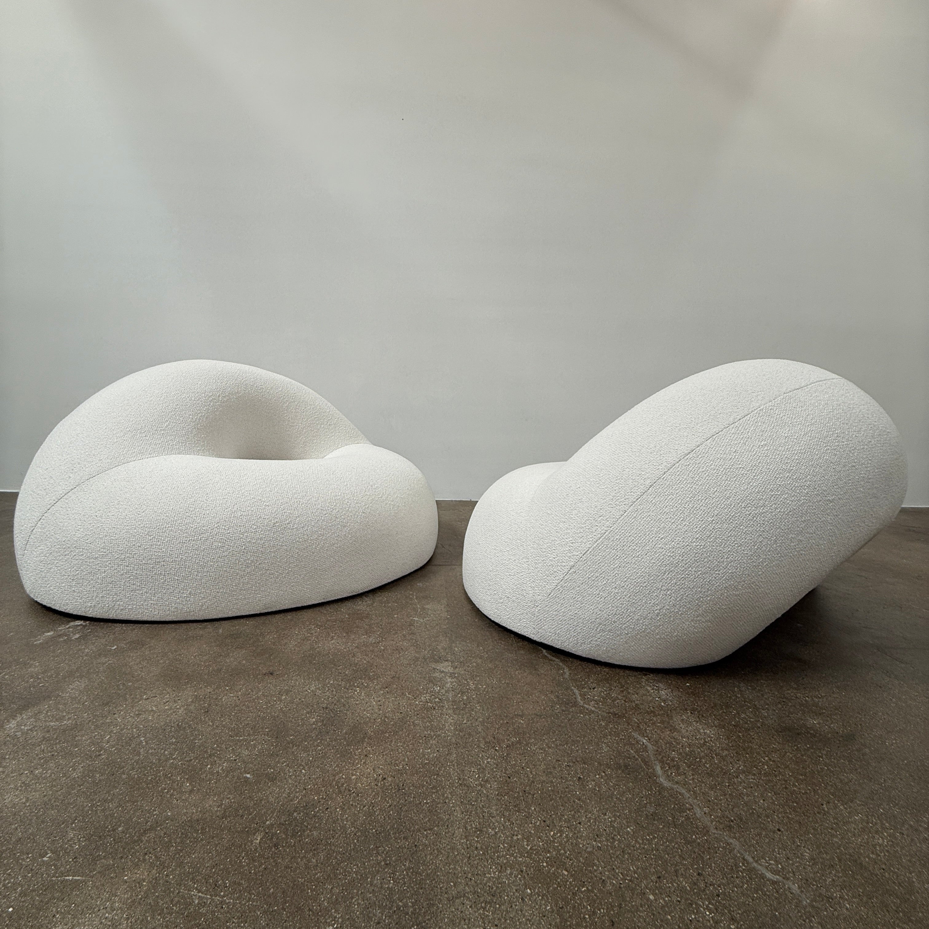 The Objects of Common Interest Tube Chair by Objects of Common Interest is a modern, light grey lounge chair with a donut-shaped design, rounded form, and central indentation, shown against a plain white background.