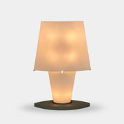 The Fontana Arte 3064 Table Light by Fontana Arte, echoing Daniela Puppa's designs, boasts a wide conical shade for a warm glow. It sits elegantly on a white surface against a plain backdrop, capturing the essence of postmodern art.