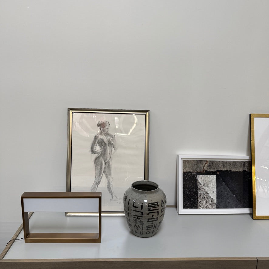 The Arterior Aura LED Table Lamp in Antique Brass by Arterior is paired with a modern console table featuring a gold rectangular frame and single white drawer, set against a plain white background.
