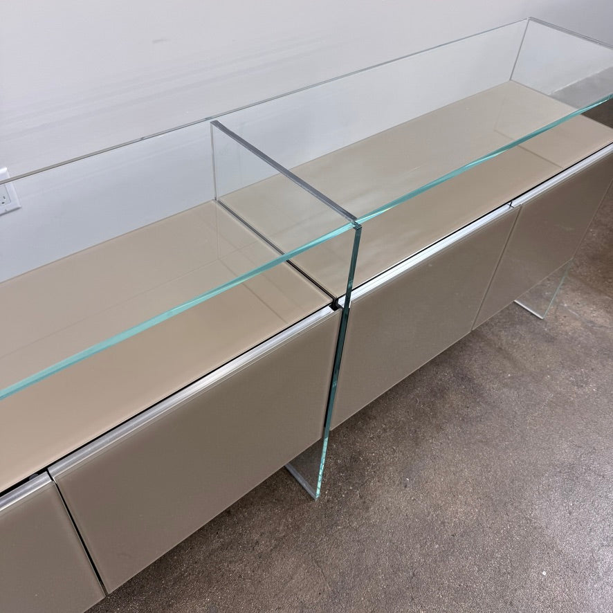 A long Gallotti & Radice Air Console Table featuring a clear glass frame and four opaque taupe storage cabinets.