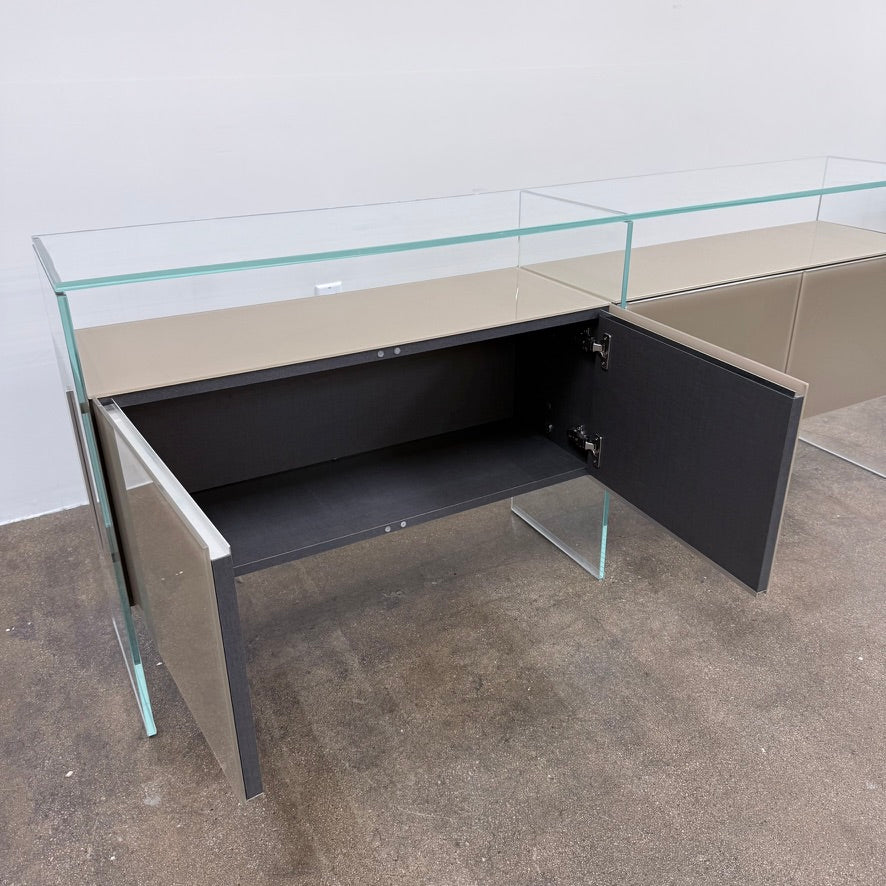 A long Gallotti & Radice Air Console Table featuring a clear glass frame and four opaque taupe storage cabinets.
