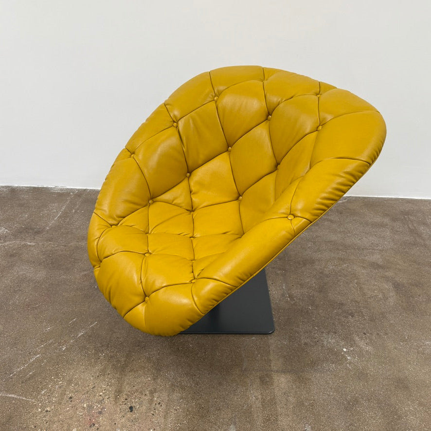 The Moroso Bohemian Low Armchair by Moroso features mustard yellow tufted leather upholstery, a matching cushion, and a black metal pedestal base, shown against a plain white background.