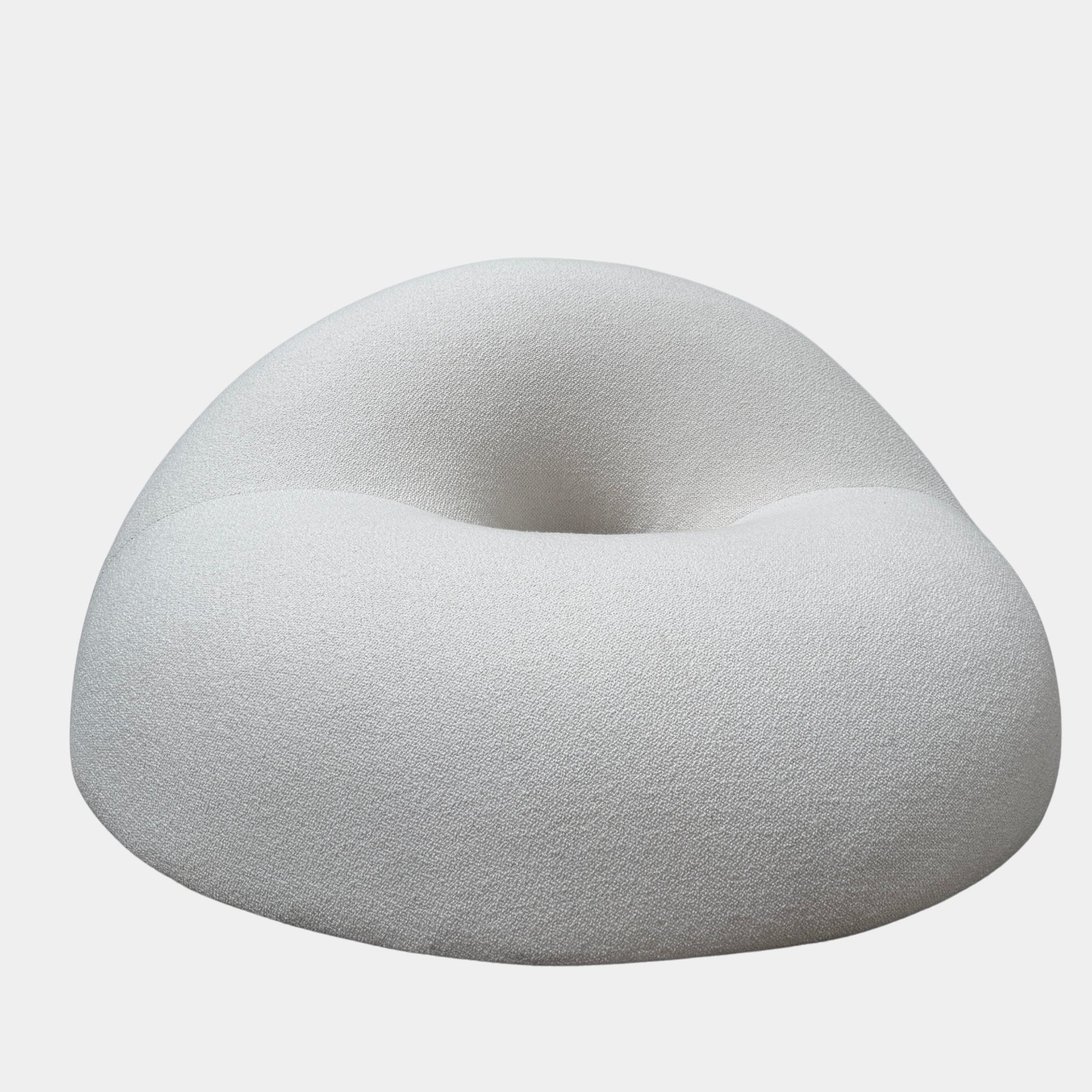 The Objects of Common Interest Tube Chair by Objects of Common Interest is a modern, light grey lounge chair with a donut-shaped design, rounded form, and central indentation, shown against a plain white background.