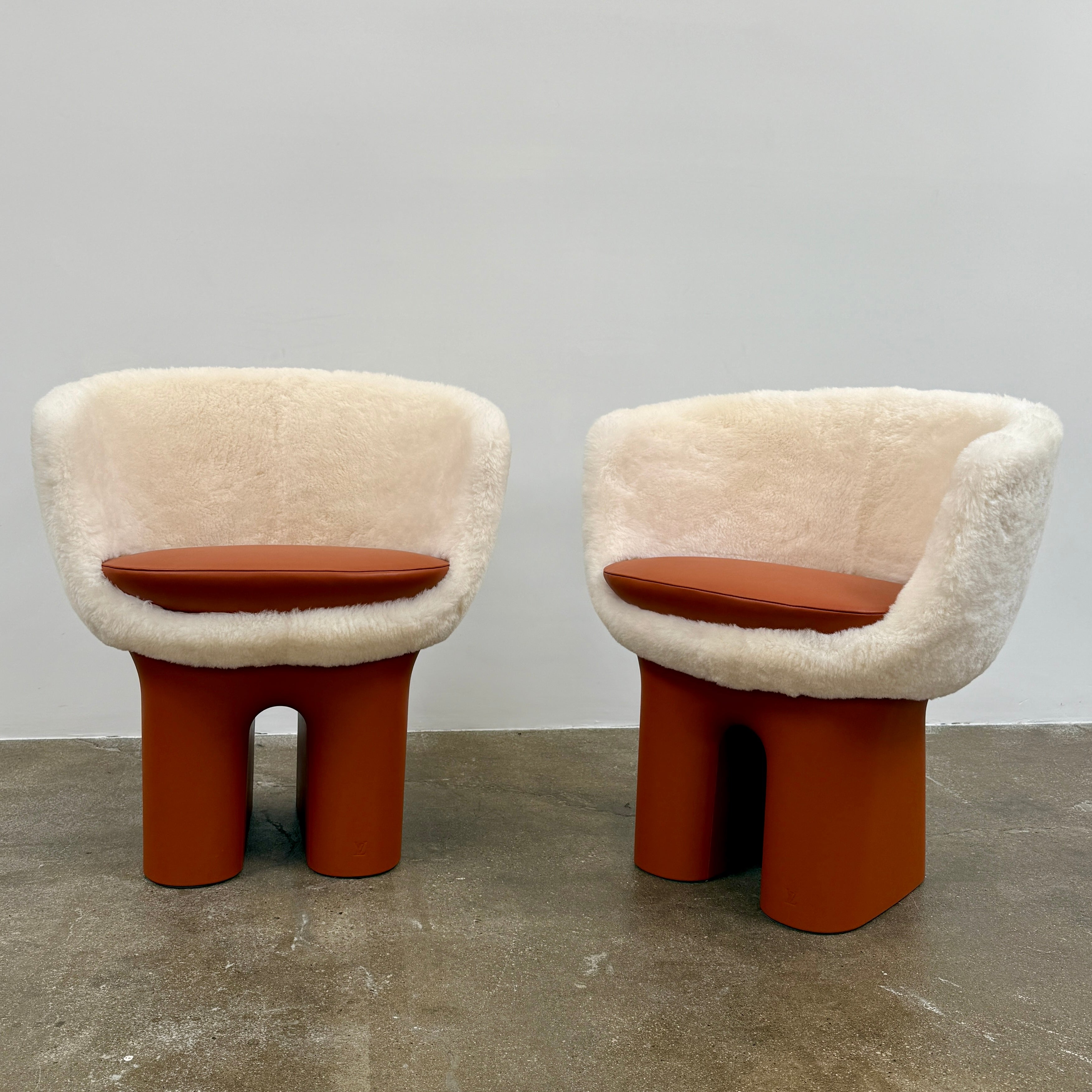 The Louis Vuitton Dolls Fur by Raw Edges is a modern chair with a curved white fluffy leather and fur seat, two short cylindrical brown legs, and a matching brown base, designed by Louis Vuitton and set against a plain background.
