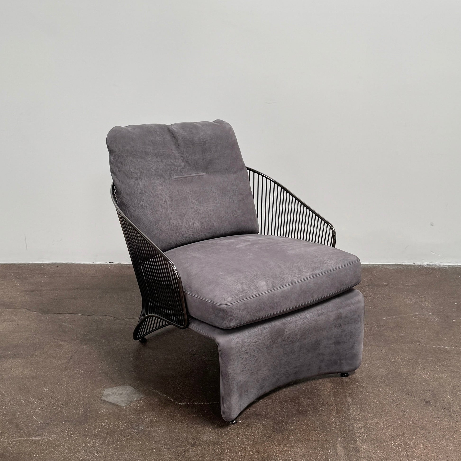 A set of two Minotti Colette Lounge Chairs by Minotti is displayed side by side against a plain white background. Each chair showcases luxurious gray nubuck leather upholstery and sleek black metal armrests, elegantly capturing the timeless mid-century silhouette characteristic of the iconic design.