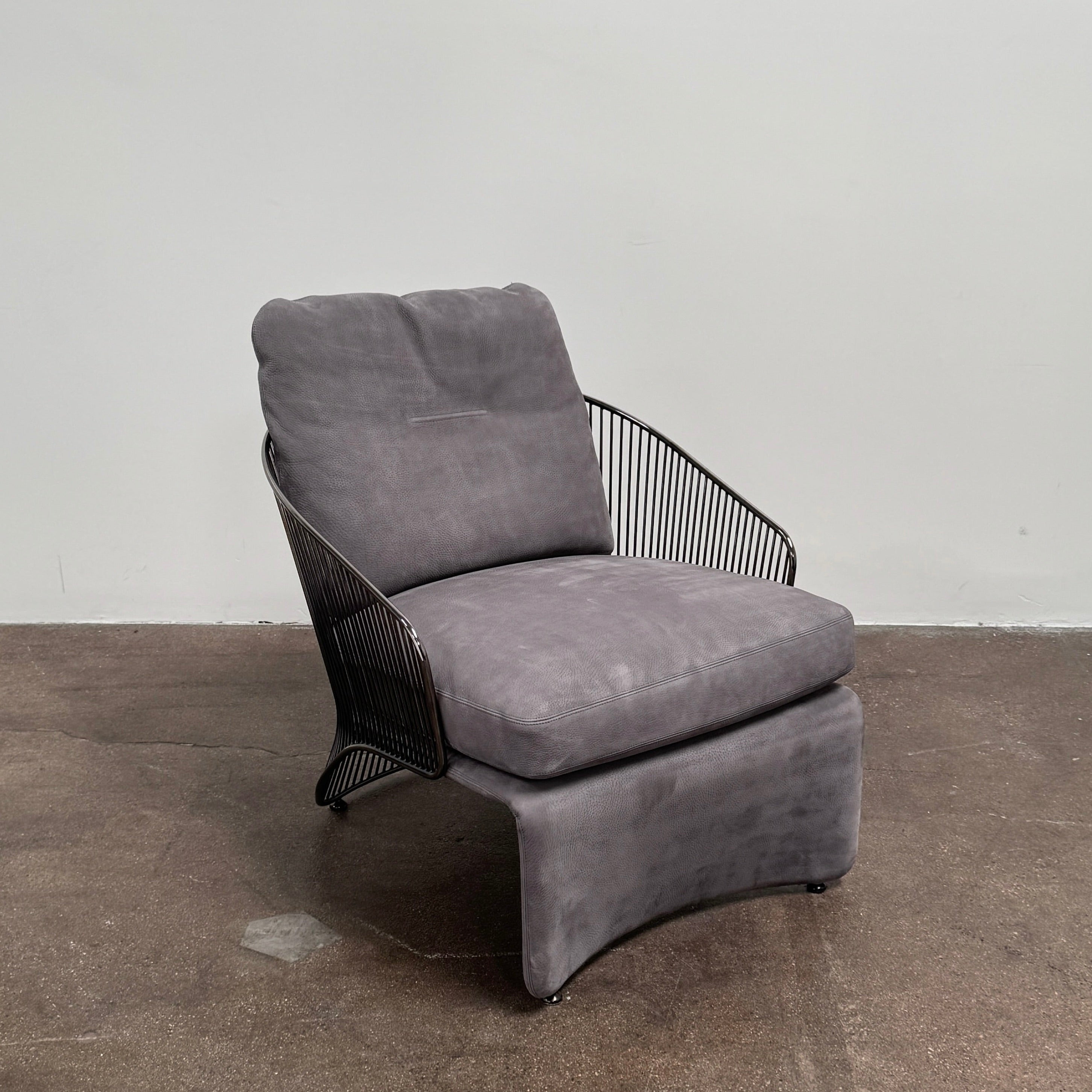 A set of two Minotti Colette Lounge Chairs by Minotti is displayed side by side against a plain white background. Each chair showcases luxurious gray nubuck leather upholstery and sleek black metal armrests, elegantly capturing the timeless mid-century silhouette characteristic of the iconic design.
