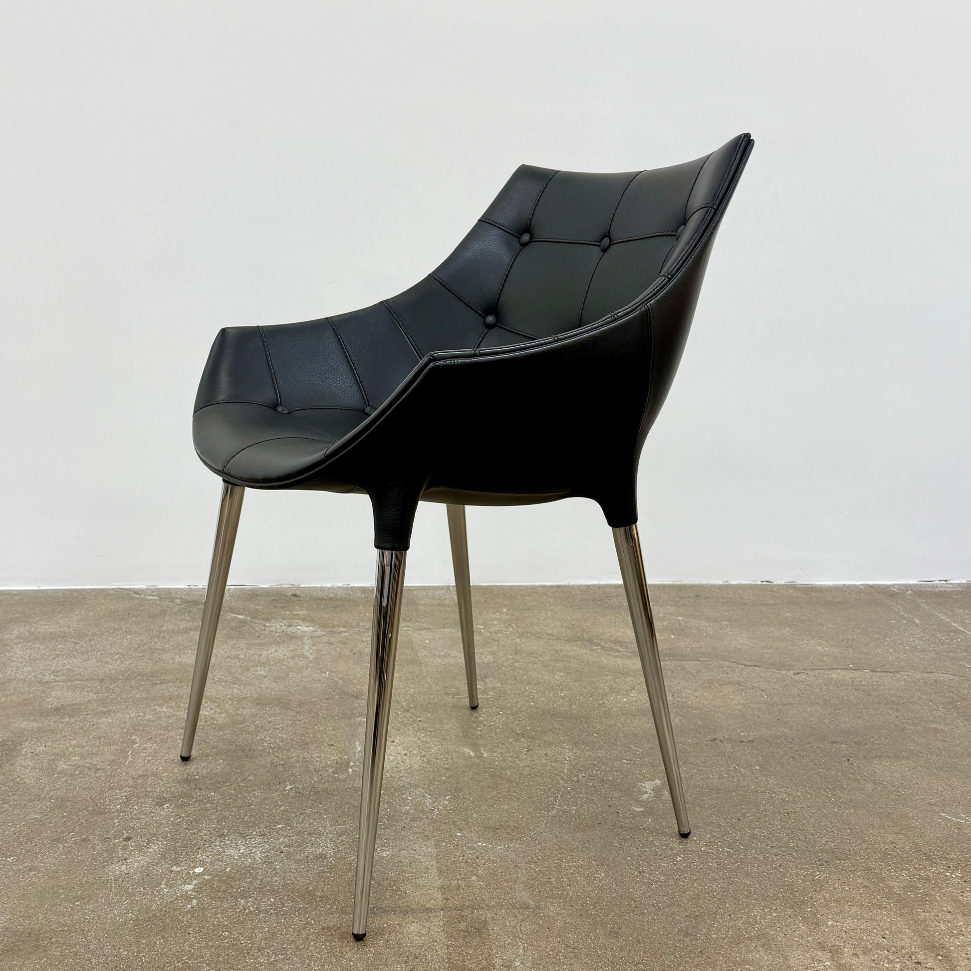 The Cassina Passion Side Chair by Cassina is a modern black upholstered chair with a curved backrest, button detailing, and four sleek metal legs inspired by the Passion design.