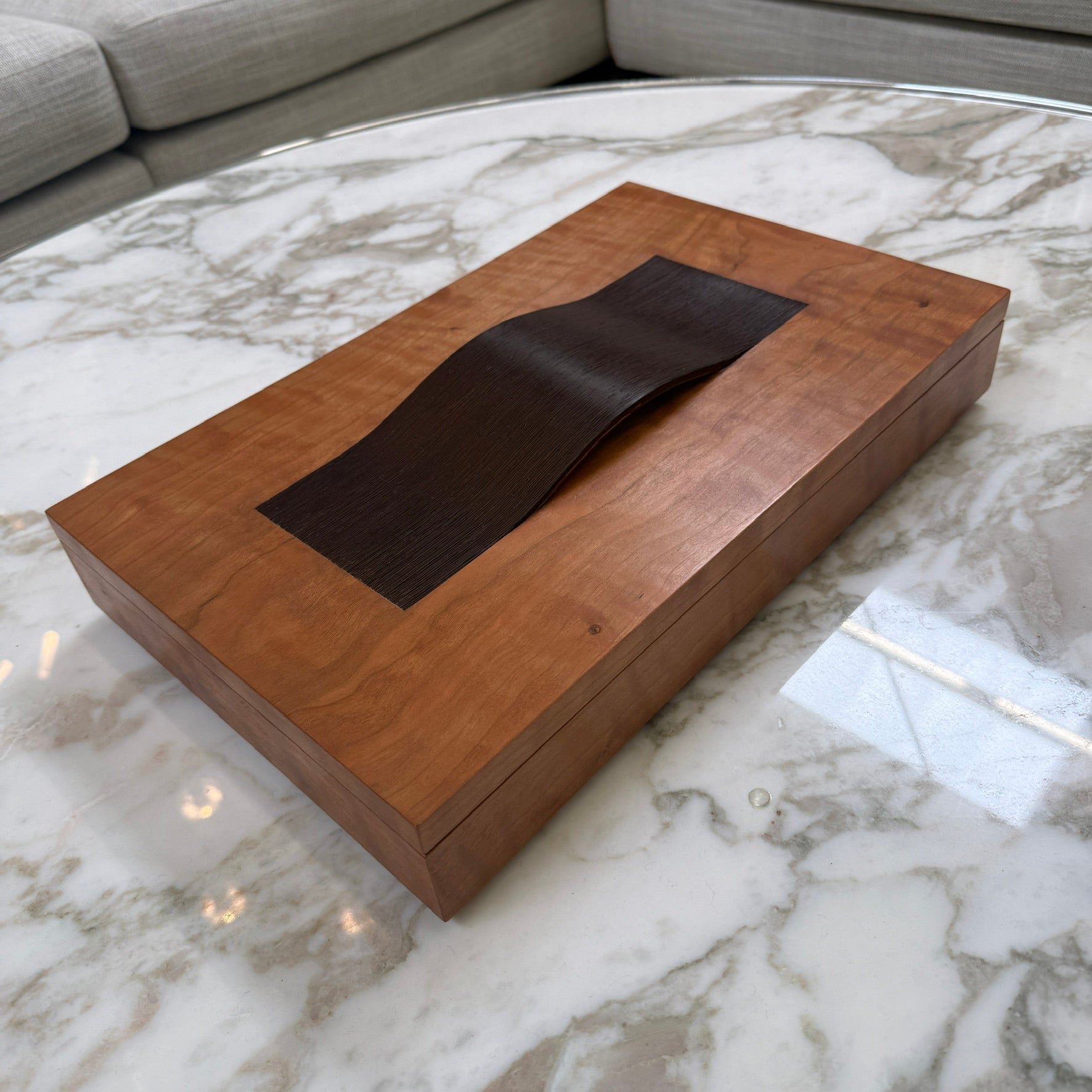 The Mike Fair Jewelry Box / Cigar Box by Mike Fair Custom Furnishings is a rectangular cherry wood box with a smooth finish and a curved, dark handle on the lid, displayed against a plain white background.