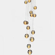 The Bocci 14.14 Pendant Chandelier by Bocci features a vertical cluster of metallic pendants, each with a glowing bulb, suspended by thin cords against a white background for a modern look.