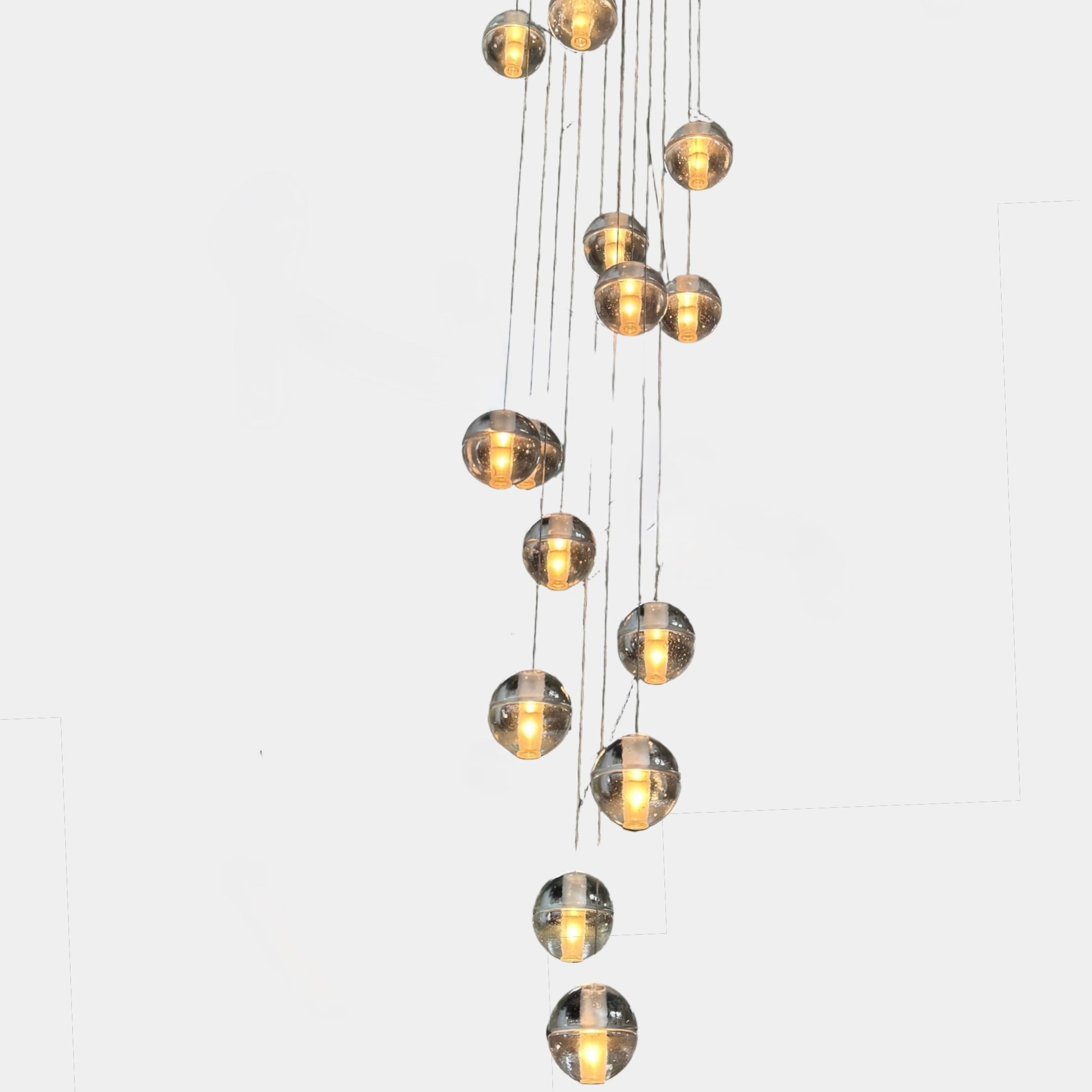 The Bocci 14.14 Pendant Chandelier by Bocci features a vertical cluster of metallic pendants, each with a glowing bulb, suspended by thin cords against a white background for a modern look.