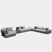 The Minotti West Sectional Sofa with Side Table and Clive Bench by Minotti features a large, L-shaped modern design with gray upholstery, multiple plush cushions, and an integrated side table—perfect for elevating luxury living rooms—all set against a plain white background.