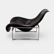 A B&B Italia Mart Relax Armchair with Tilting Mechanism in black saddle leather features a modern, curved design and is set on a polished concrete floor against a plain light gray wall.