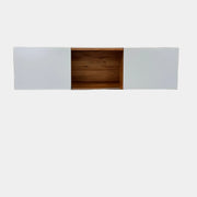 A Modern Resale Mash Studios LAX series 3X Wall Mounted Shelf in natural ash wood and matte white is mounted against a plain wall above a concrete floor, featuring a white exterior with wood-toned interior shelving.
