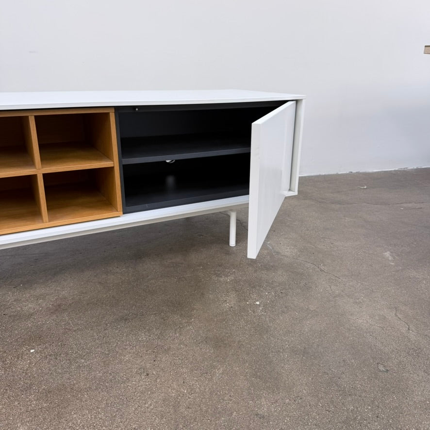 Low-profile white DWR Treku Aura Media Unit on thin legs, featuring two side cabinets and a central open shelf section with a wood-toned interior.