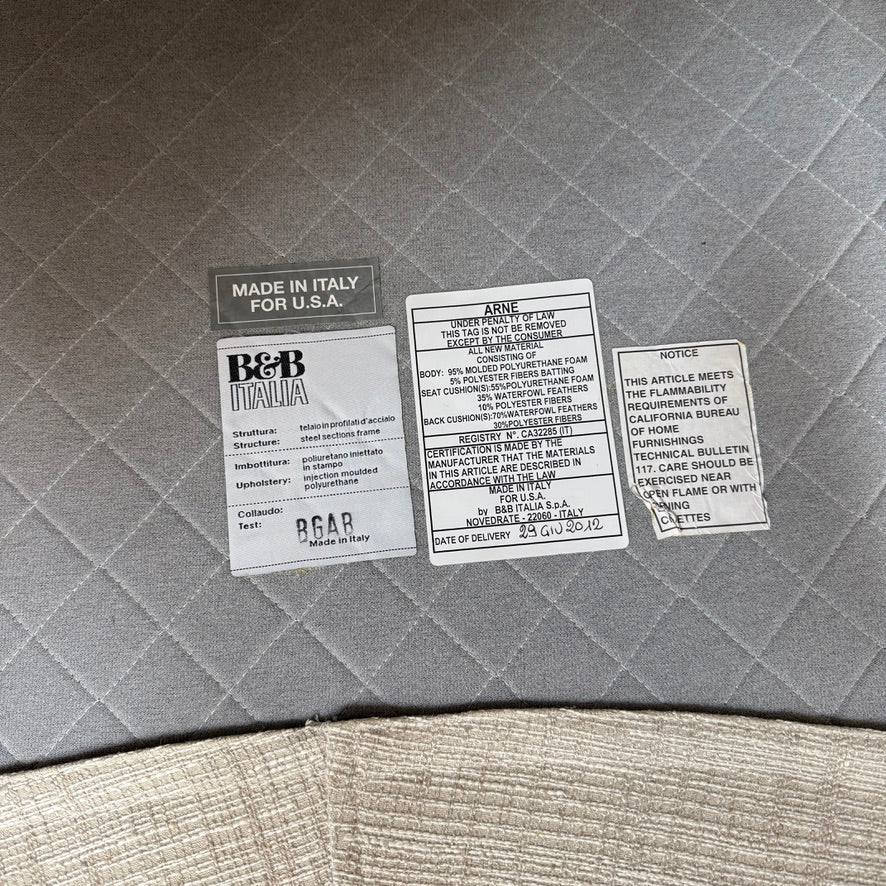 Experience the B&B Italia Arne Sofa, a modern off-white masterpiece with five plush cushions and cylindrical armrests. Designed by Antonio Citterio, it features sleek metal legs set against a crisp background.