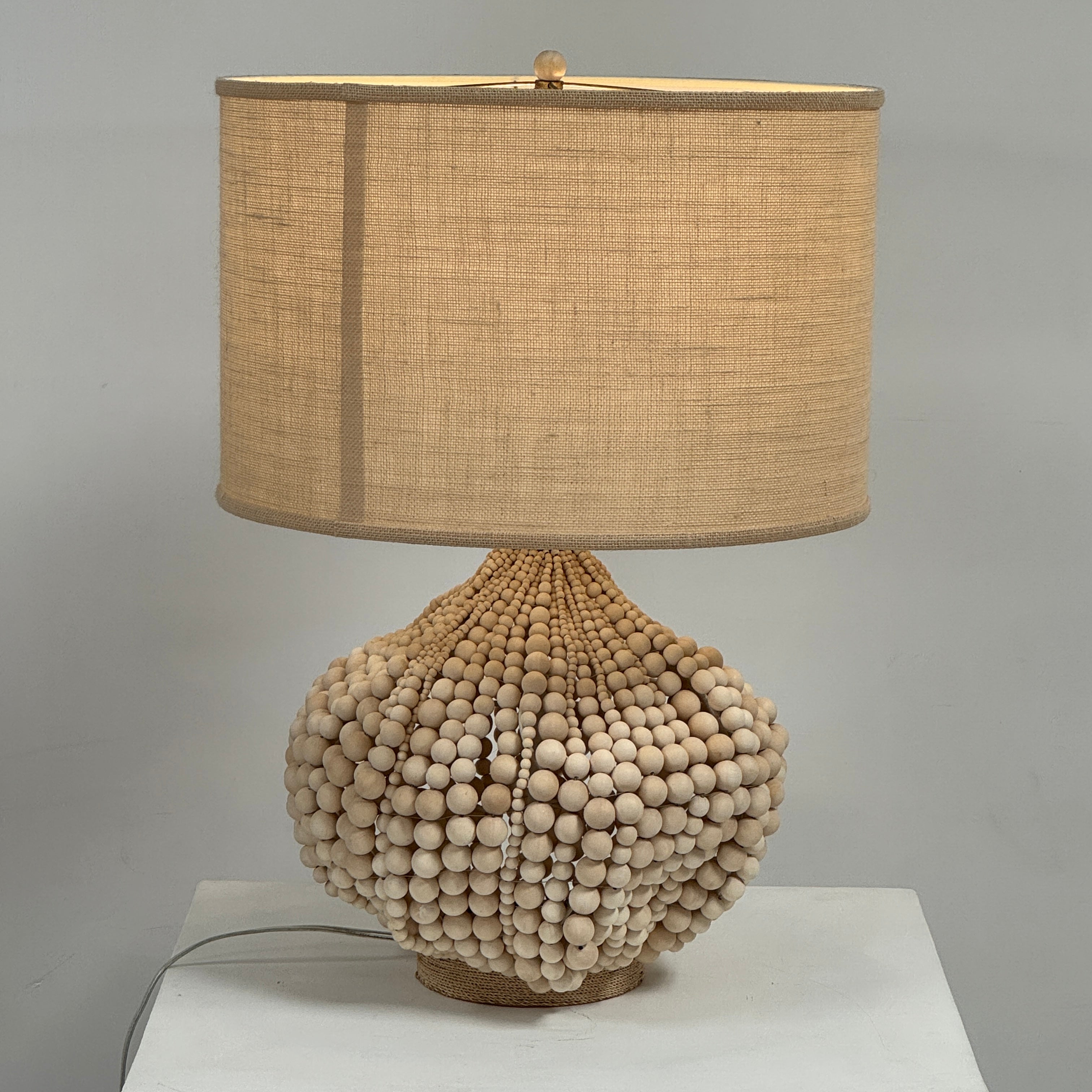 The Palecek Point Dume Table Lamp by Palecek features a clustered wooden bead base and a cylindrical beige fabric shade, offering relaxed coastal elegance for your space.