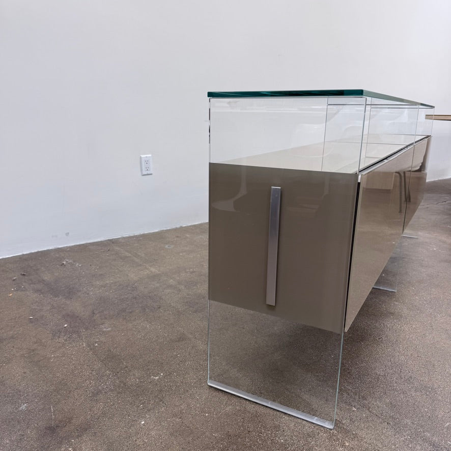 A long Gallotti & Radice Air Console Table featuring a clear glass frame and four opaque taupe storage cabinets.