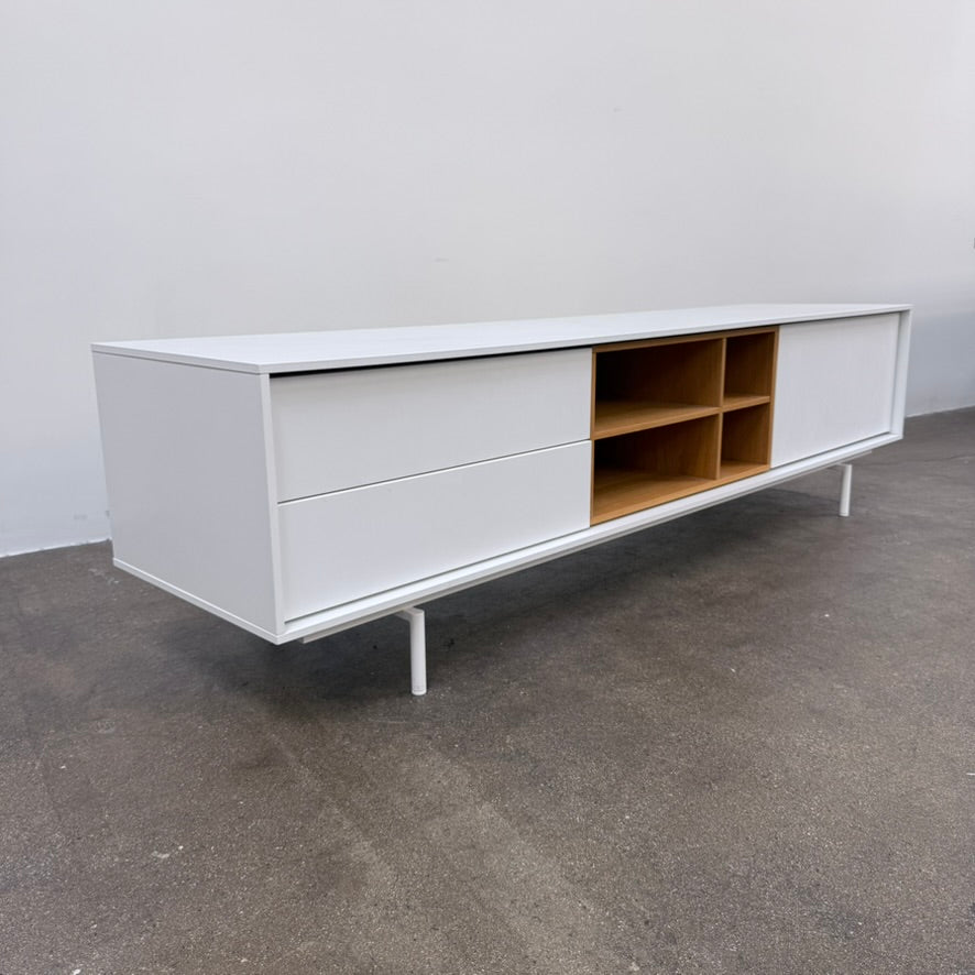 Low-profile white DWR Treku Aura Media Unit on thin legs, featuring two side cabinets and a central open shelf section with a wood-toned interior.