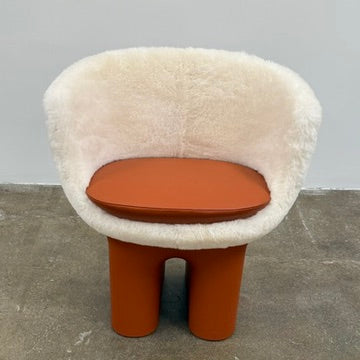 The Louis Vuitton Dolls Fur by Raw Edges is a modern chair with a curved white fluffy leather and fur seat, two short cylindrical brown legs, and a matching brown base, designed by Louis Vuitton and set against a plain background.