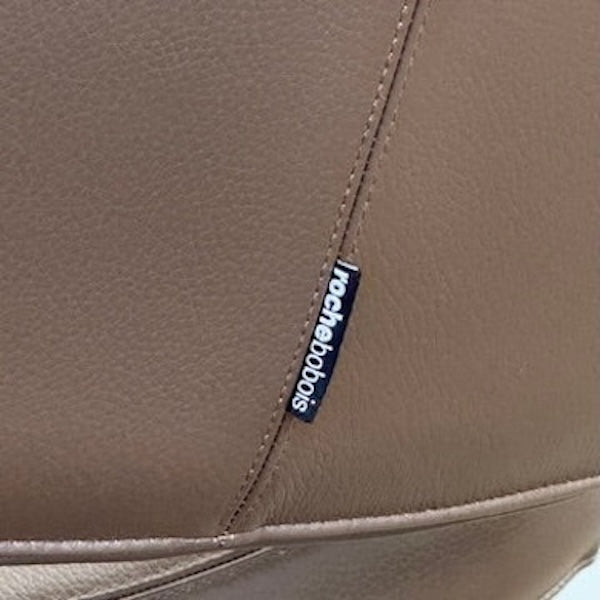 The Roche Bobois Nuage Swivel Chair is a modern, circular brown leather chair with a curved backrest and seat on a metal swivel base, set on a concrete floor against a plain white wall.