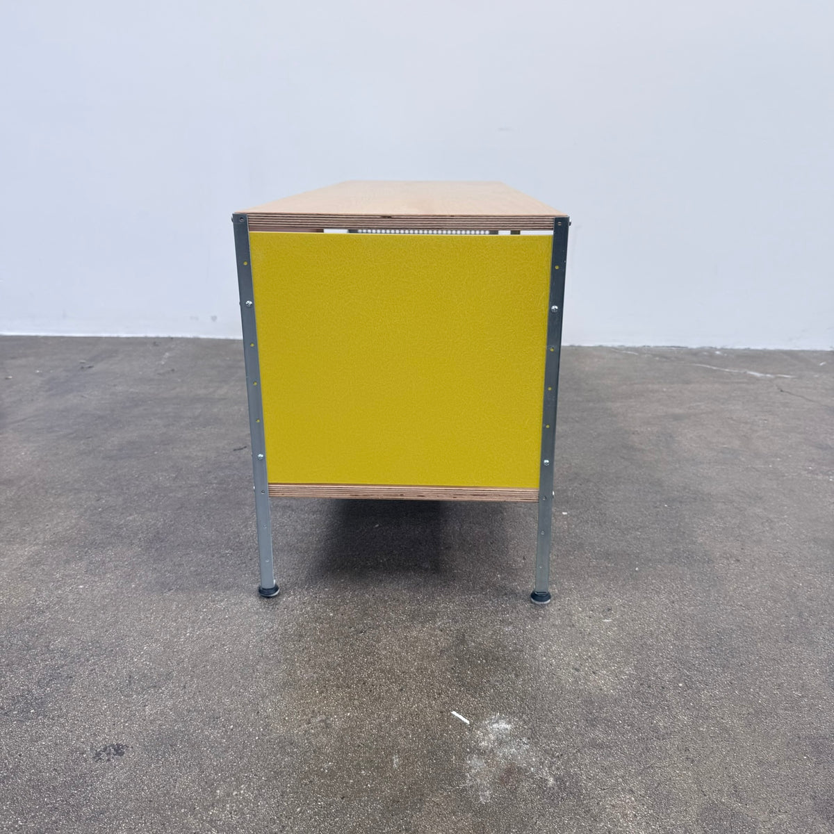 Herman Miller Eames Storage Unit featuring a low rectangular frame with plywood shelves, a yellow side panel, a pink back panel, and a perforated metal side.