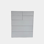 The Treku Lauki Tall Dresser by Treku, with a sleek lacquered finish and push-latch drawers—one partially open—stands on a concrete floor against a plain white wall.