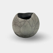 The Sofi Ceramic Raku Small Vessel by Sofi Ceramics is a round, grey ceramic vase with a marble crack-like pattern, drawing inspiration from textured African cultural vessels, and it features a wide, uneven opening against a plain white background.