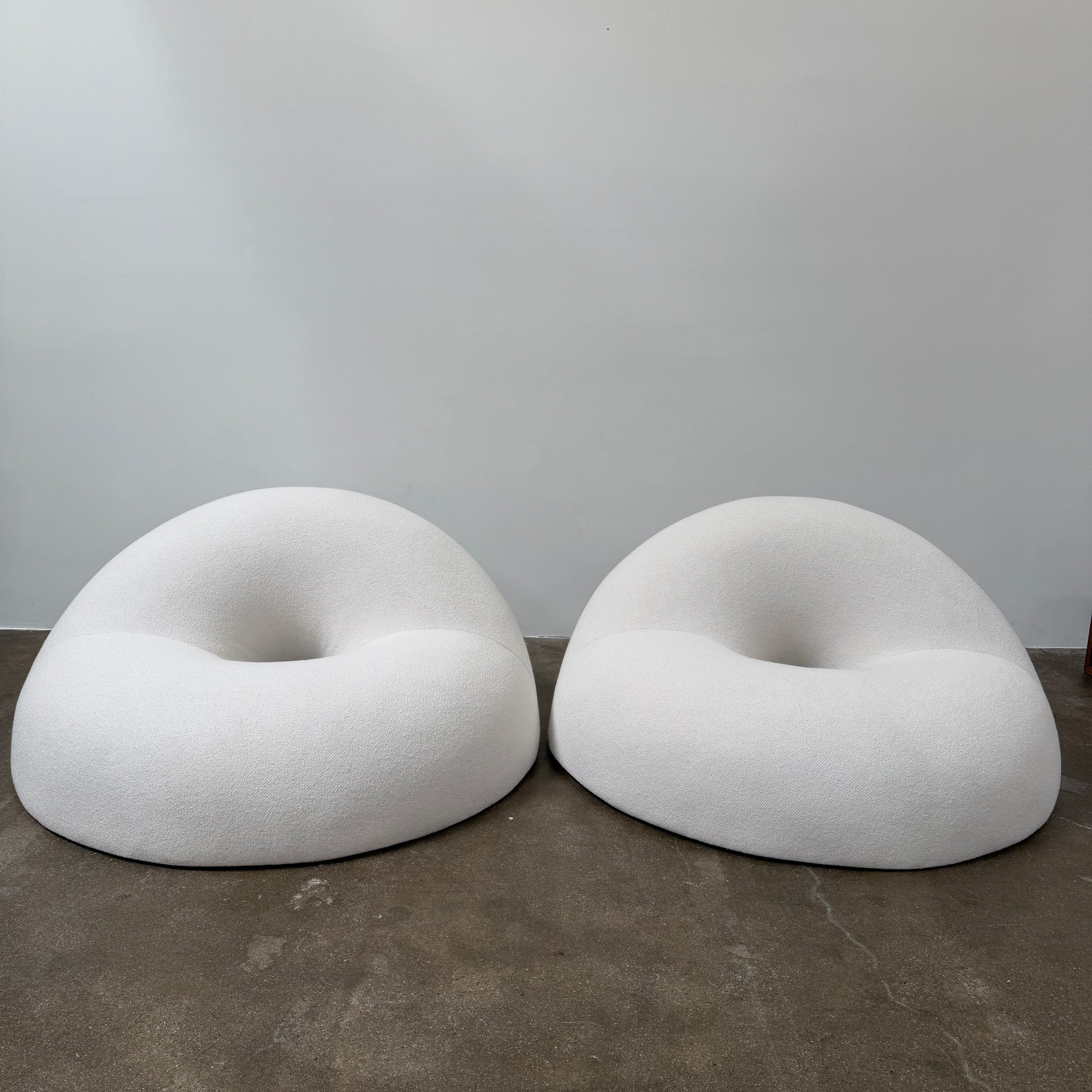 The Objects of Common Interest Tube Chair by Objects of Common Interest is a modern, light grey lounge chair with a donut-shaped design, rounded form, and central indentation, shown against a plain white background.