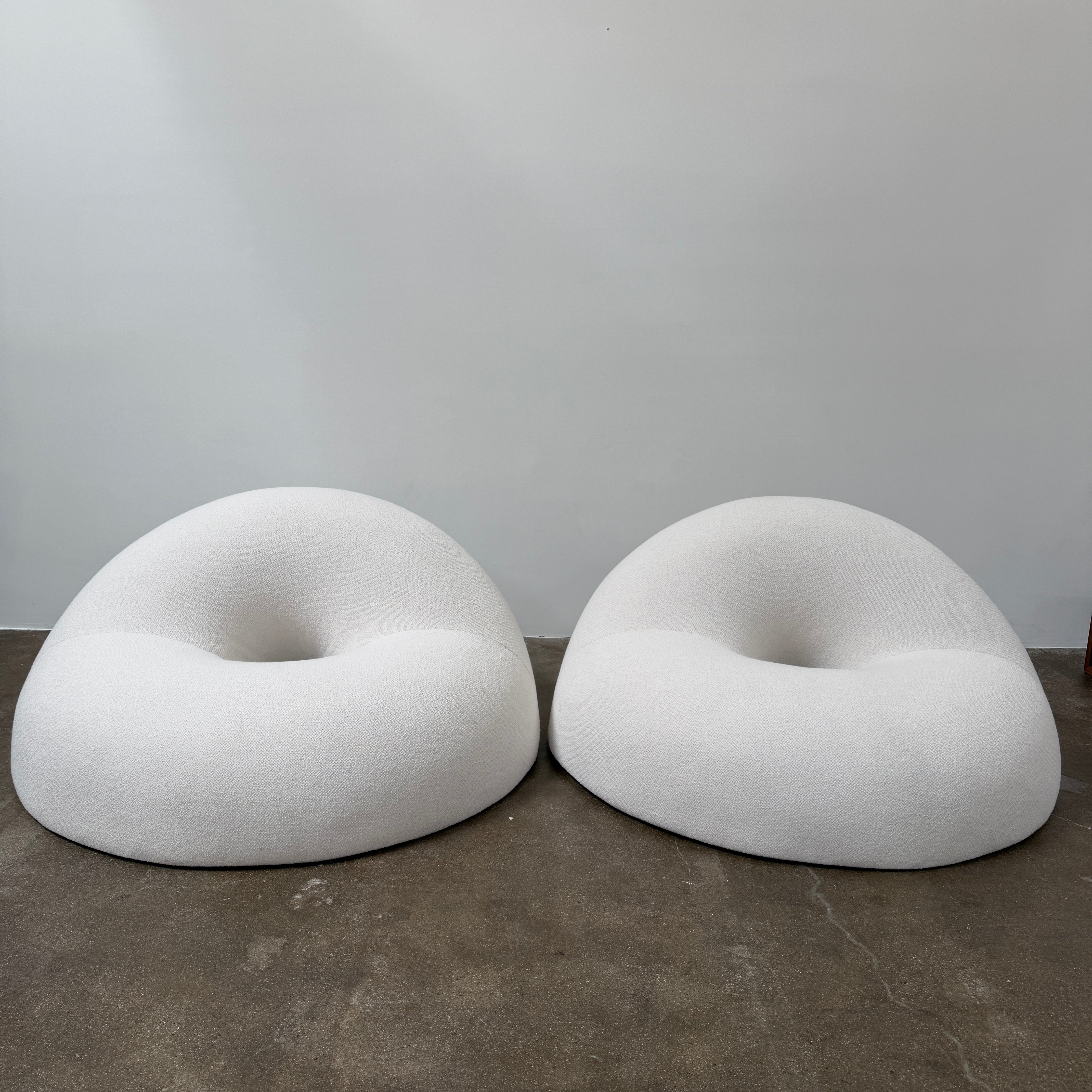 The Objects of Common Interest Tube Chair by Objects of Common Interest is a modern, light grey lounge chair with a donut-shaped design, rounded form, and central indentation, shown against a plain white background.