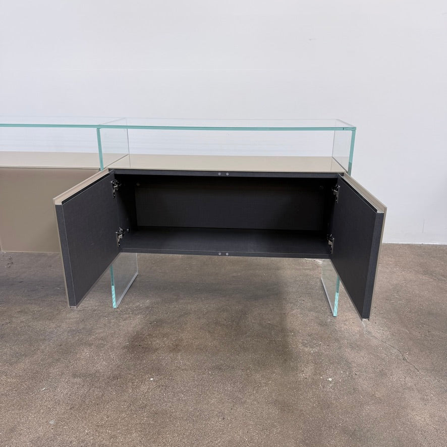 A long Gallotti & Radice Air Console Table featuring a clear glass frame and four opaque taupe storage cabinets.