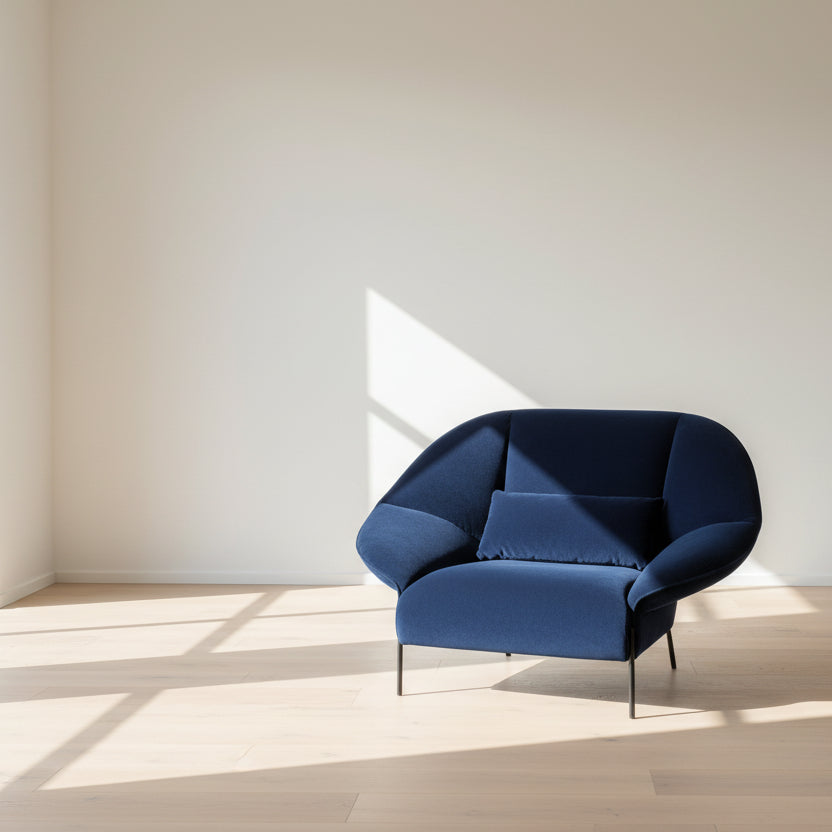 The Ligne Roset Paipai Armchair by Ligne Roset features a navy blue velvet finish, curved cocoon-like seat, matching rectangular cushion, slim black legs, and premium foam construction, displayed against a plain background.