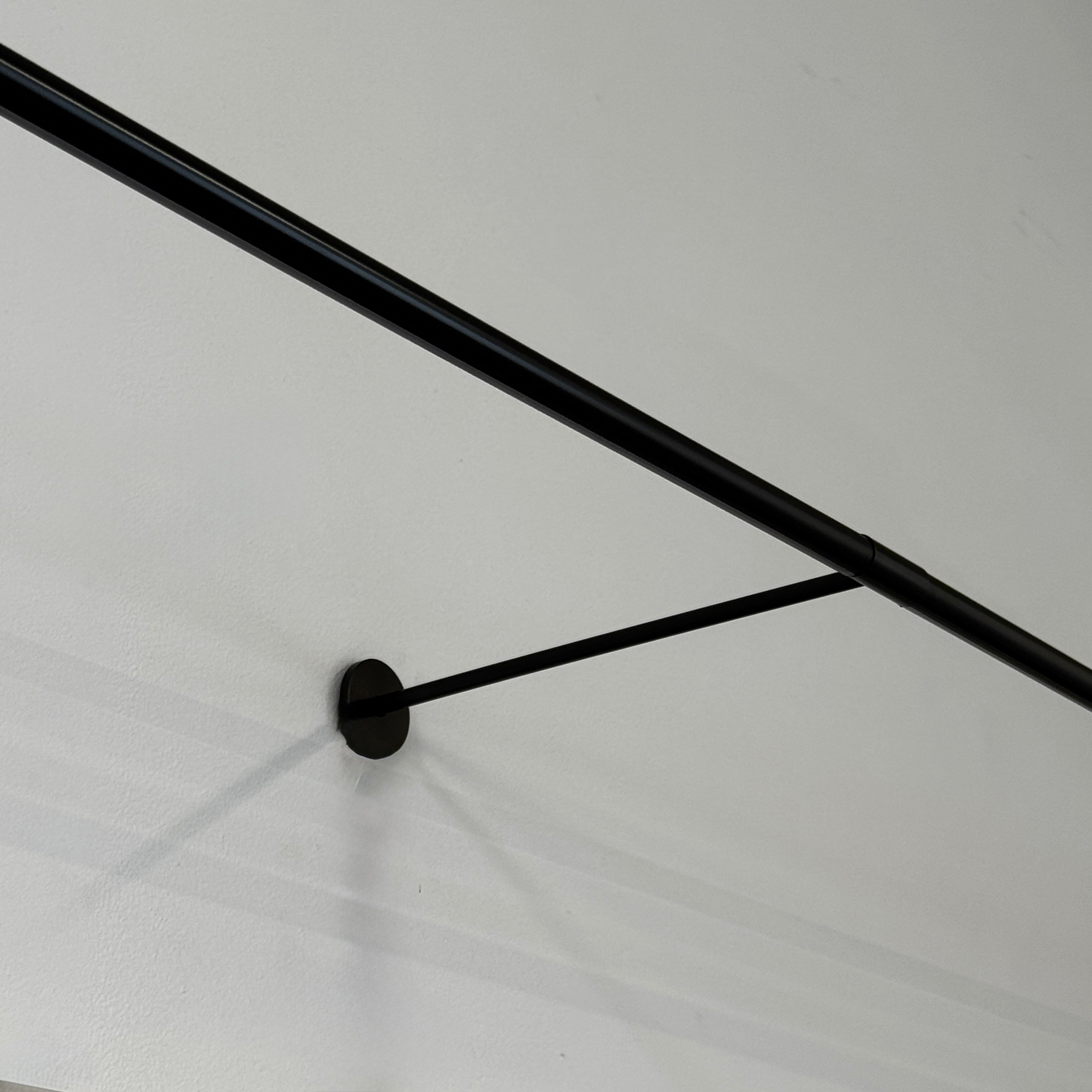 A modern abstract painting hangs on a white wall above a desk, illuminated by the Juniper THIN System Linear Light Wall-mounted from Juniper, with a lamp, documents, and office supplies arranged on the glass desktop.