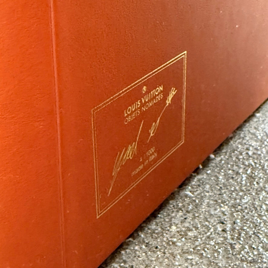 The Louis Vuitton Dolls Fur by Raw Edges is a modern chair with a curved white fluffy leather and fur seat, two short cylindrical brown legs, and a matching brown base, designed by Louis Vuitton and set against a plain background.