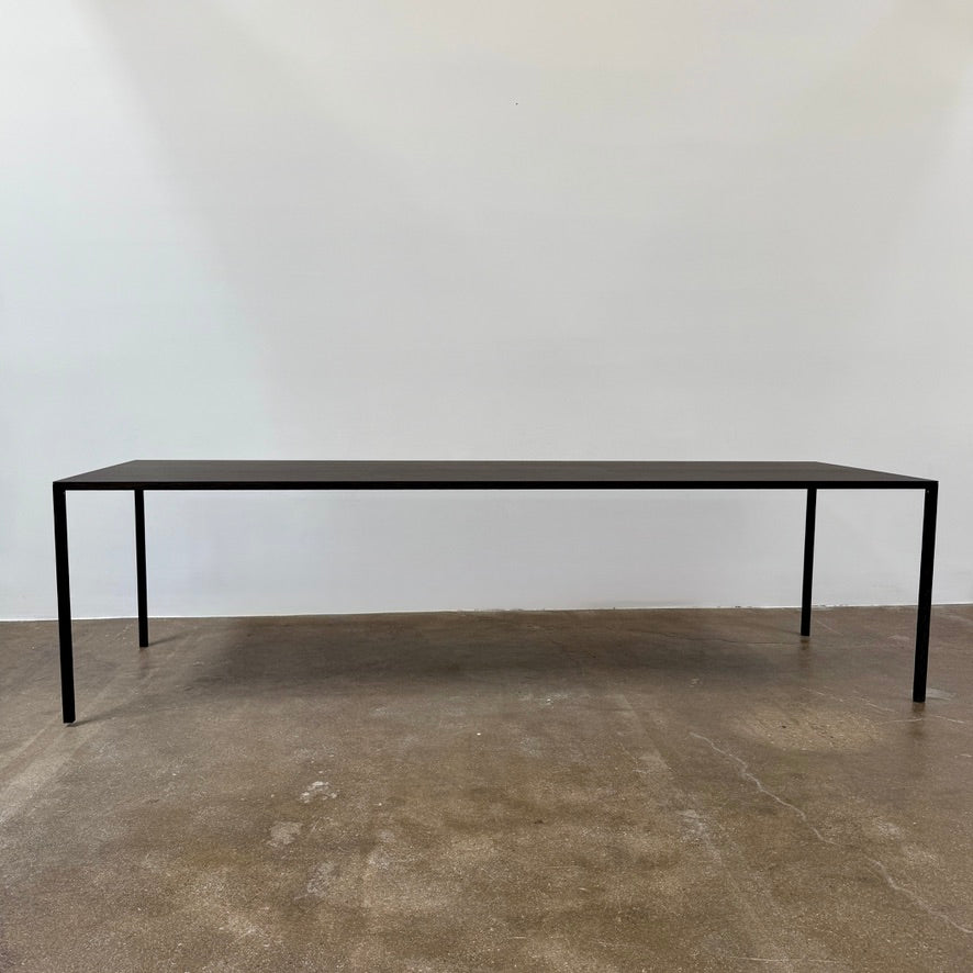 The Arco Slim Table by Arco is a minimalist rectangular table with a thin, flat surface and four slender legs, made from steel sandwich construction with a lightweight honeycomb core, shown against a plain white background.