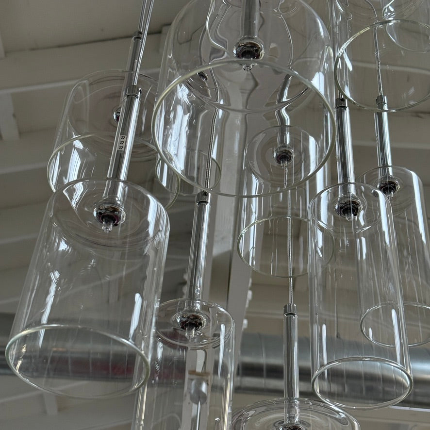 The Axo 12 Light Spillray Suspension Light by Modern Resale features cylindrical glass pendants and hangs from a high ceiling with exposed beams and fluorescent lighting.