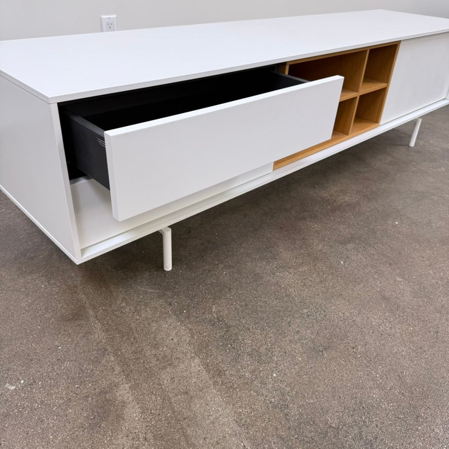 Low-profile white DWR Treku Aura Media Unit on thin legs, featuring two side cabinets and a central open shelf section with a wood-toned interior.