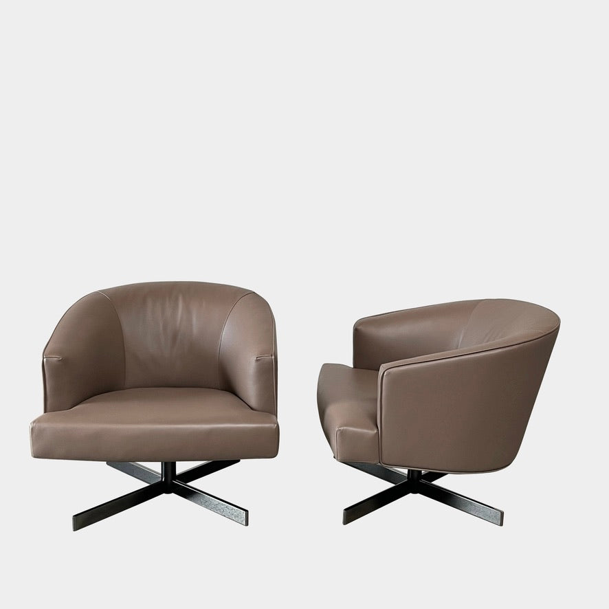 A Minotti Martin Brown Leather Swivel Chair with a cushioned seat and back, sitting on a sleek black chrome base, against a plain white background.