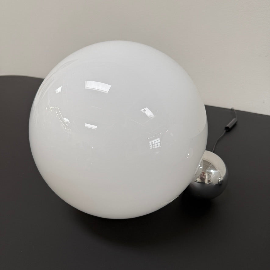 Two Flos Copycat Table Lamps by Flos, featuring glowing frosted glass spheres and chrome bases, make a sculptural statement on a dark surface against a light-colored wall.