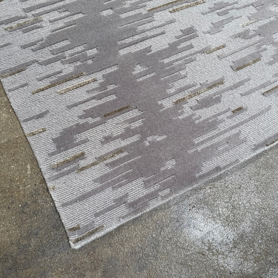 A close-up of the Kvadrat Multi-pile Wool and Silk Rug by Kvadrat, featuring an abstract linear pattern in light and dark gray wool and silk, displayed on a white background.